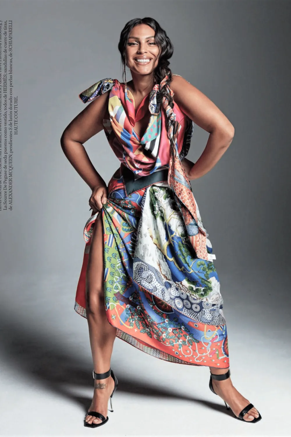 Paloma Elsesser smiling in a colorful printed dress with a draped neckline and black heels.