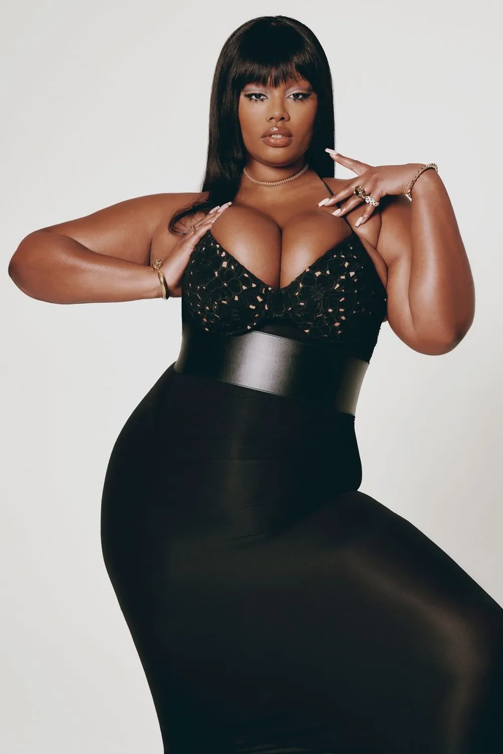 Precious Lee posing in a fitted black dress with a wide waist belt and straight dark hair.