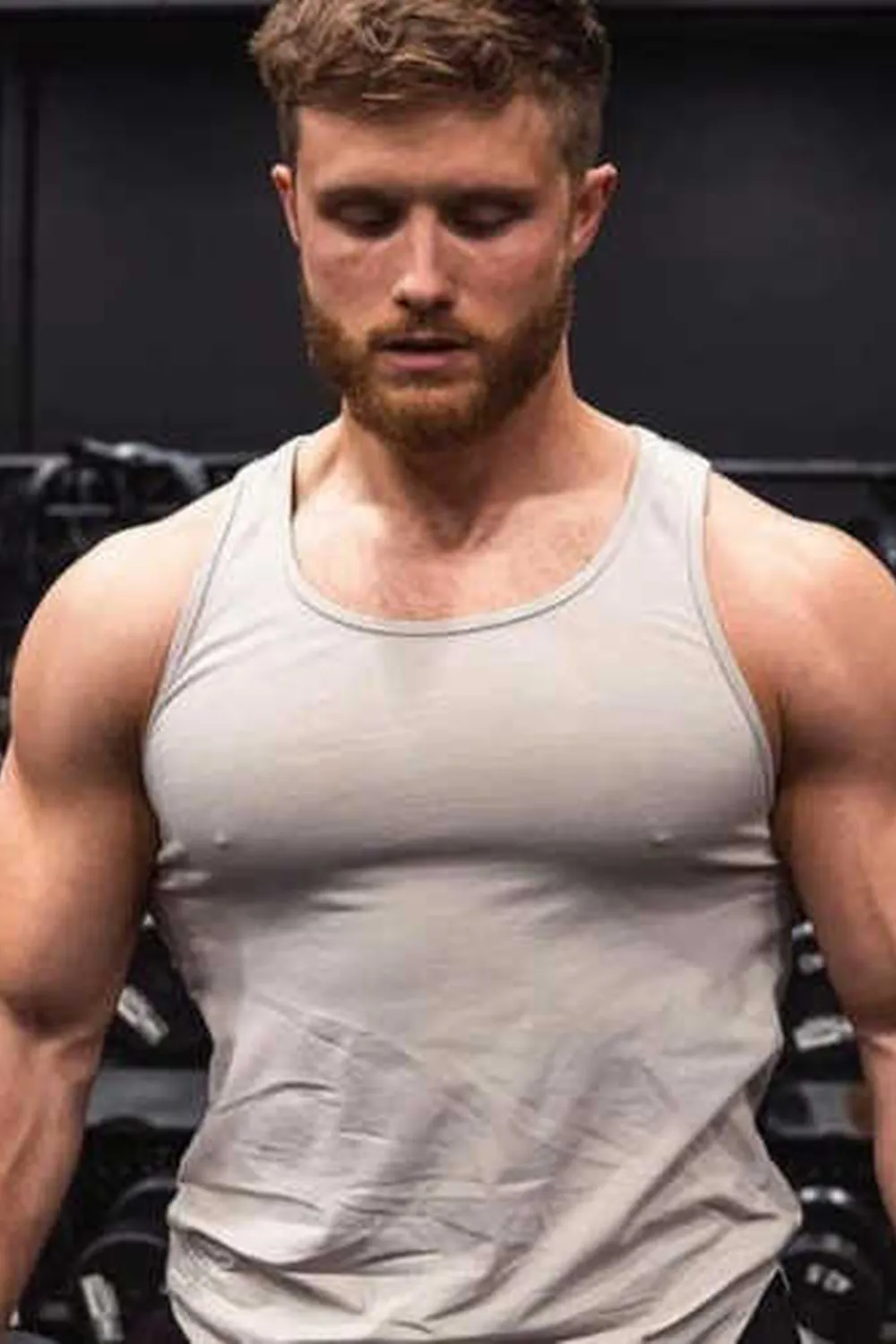 Jeff Nippard wearing a light gray tank top with gym equipment behind him.