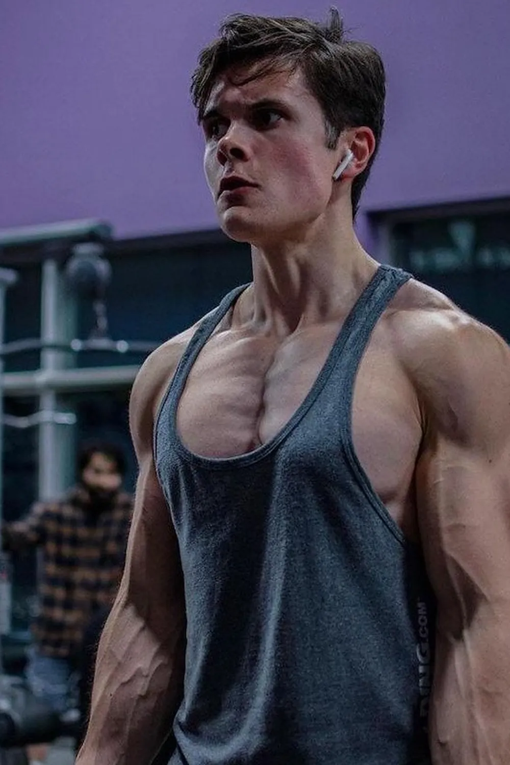 Will Tennyson wearing a gray tank top in a gym with a purple wall behind him.