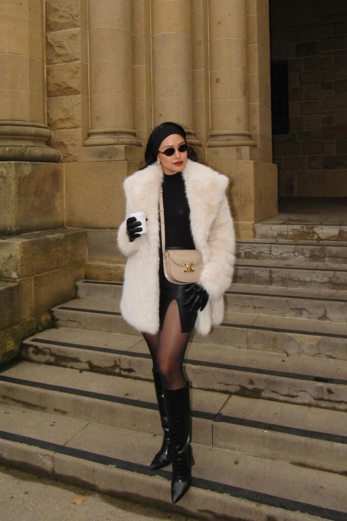 Woman in a cream coat with a black mini skirt and tall boots