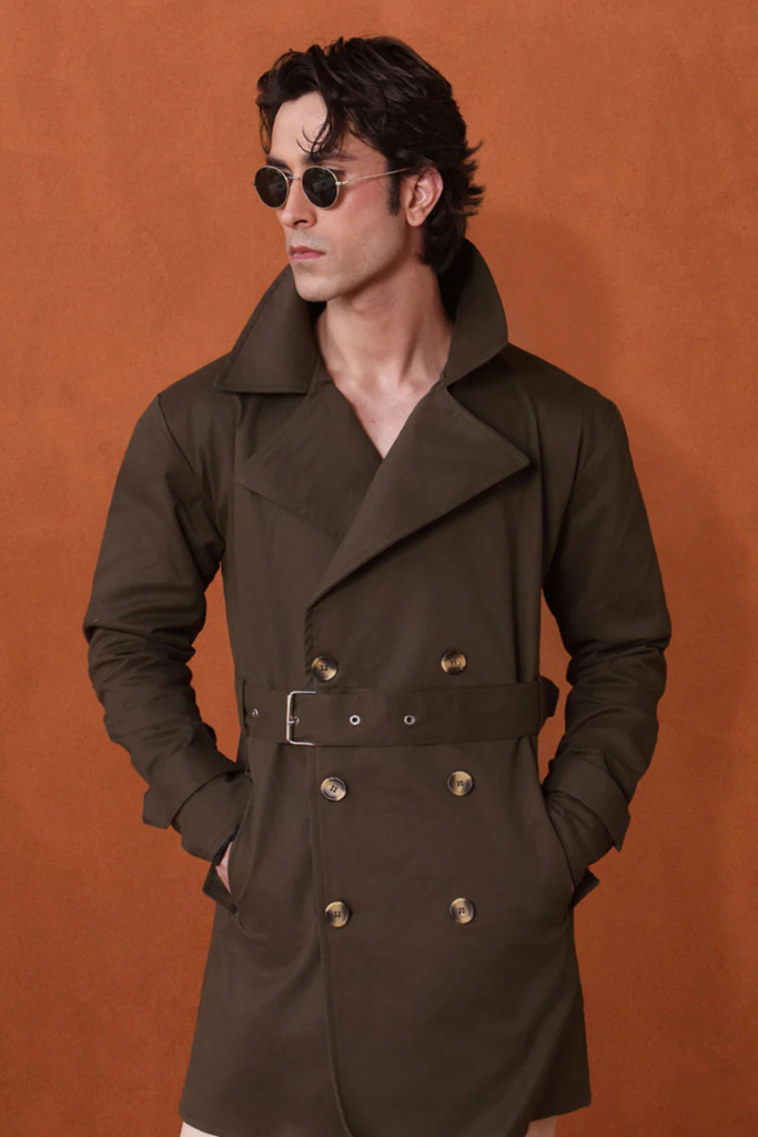 Man in a khaki green double-breasted trench coat against an orange backdrop