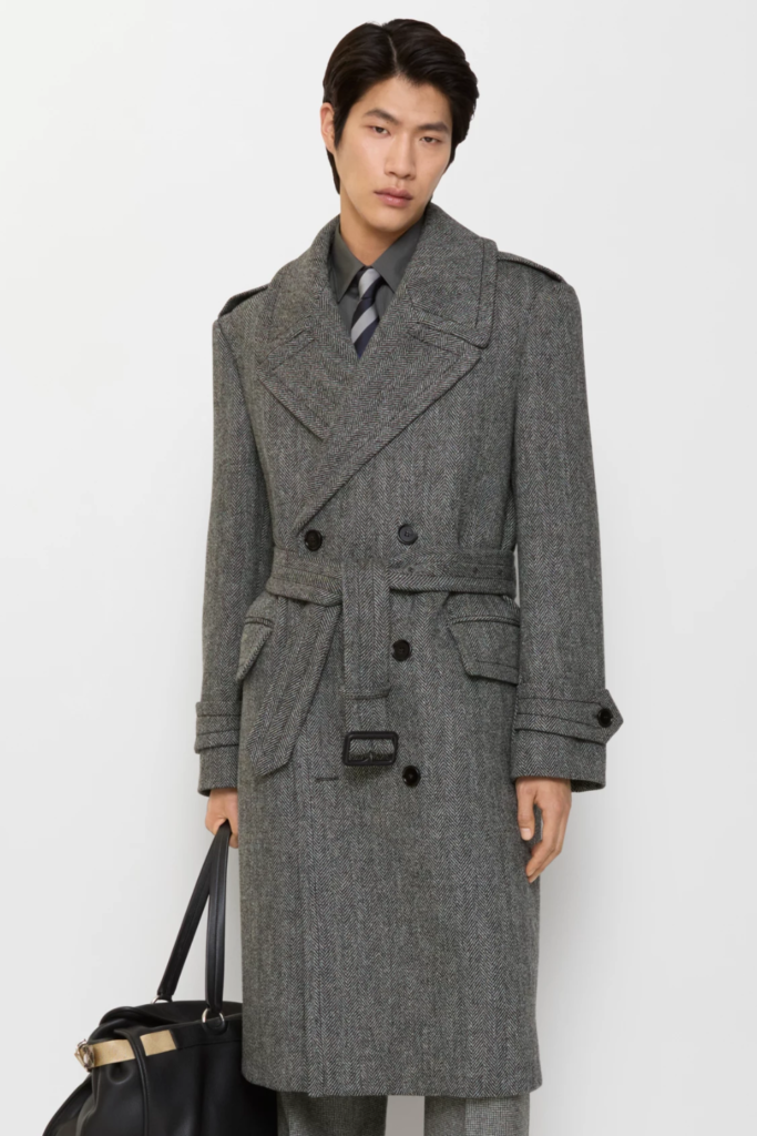 Man in a long grey herringbone wool trench coat carrying a black bag