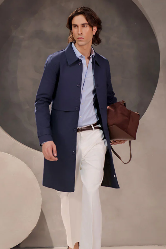 Man in a navy trench coat with white trousers, carrying a brown bag