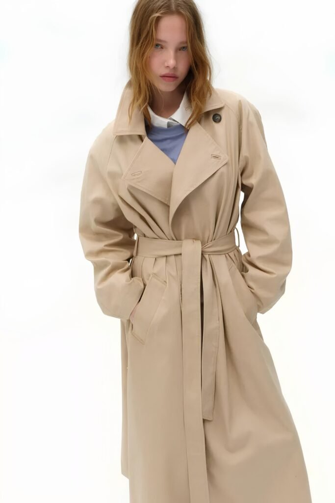 Woman in a beige trench coat with strong shoulders, belted at the waist