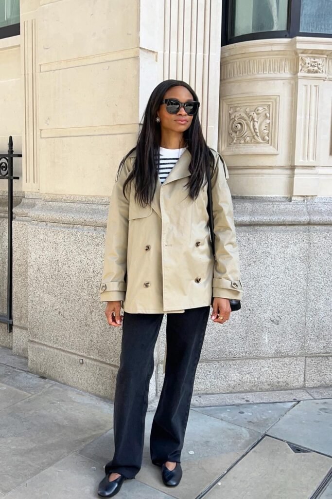 Woman in a cropped beige trench coat with a striped top and dark trousers