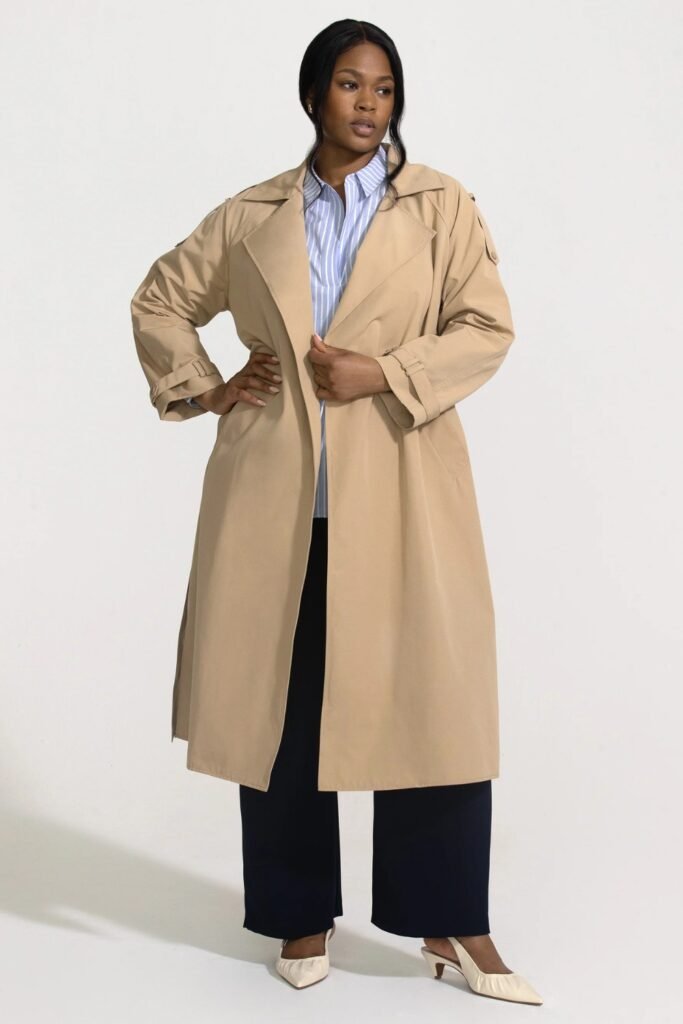 Woman in a long beige trench coat over a blue shirt and wide navy trousers