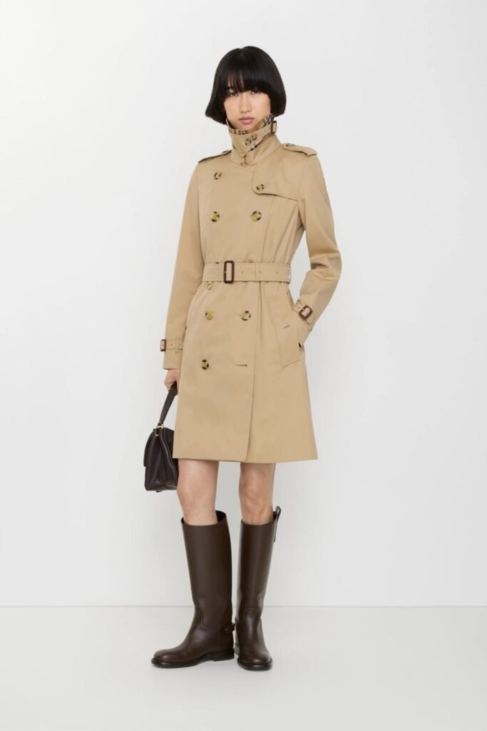 Woman in a short belted beige trench coat with tall brown boots