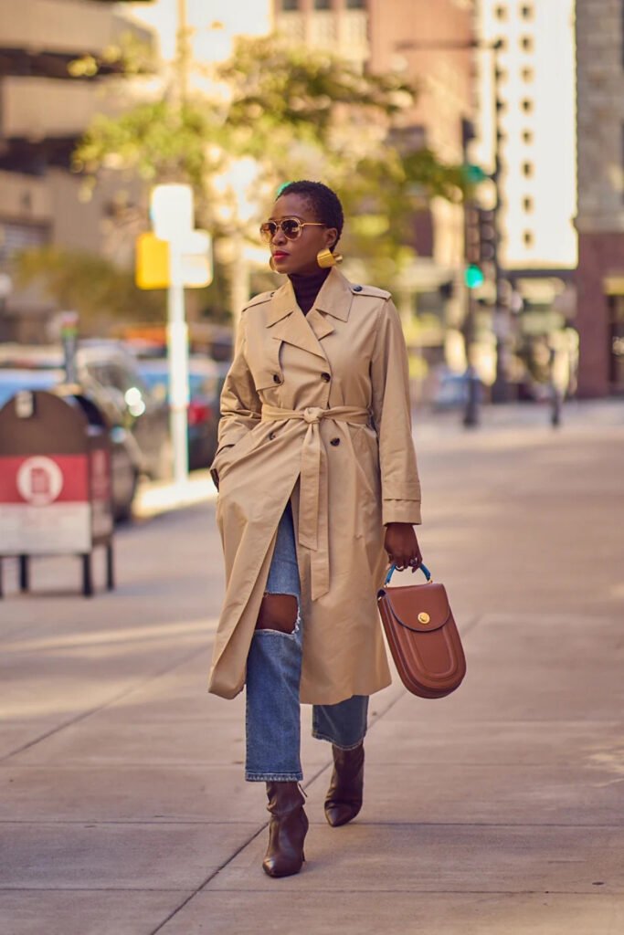 Woman in a belted trench coat with jeans and a brown bag