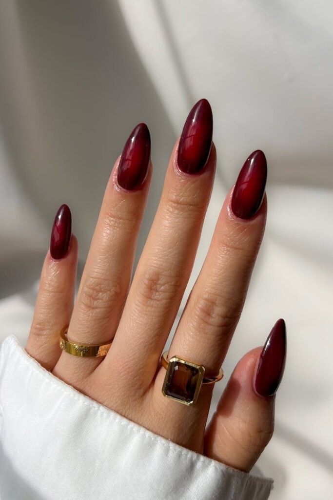 Long almond nails in deep cherry mocha worn with gold rings