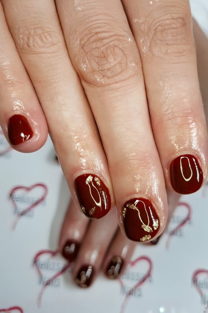 Short cherry mocha nails with gold detail beside nude accent nails
