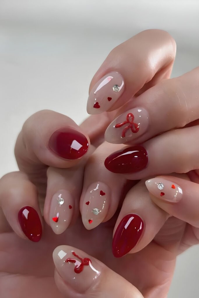 Sheer nude nails with small cherry and heart details beside solid red nails