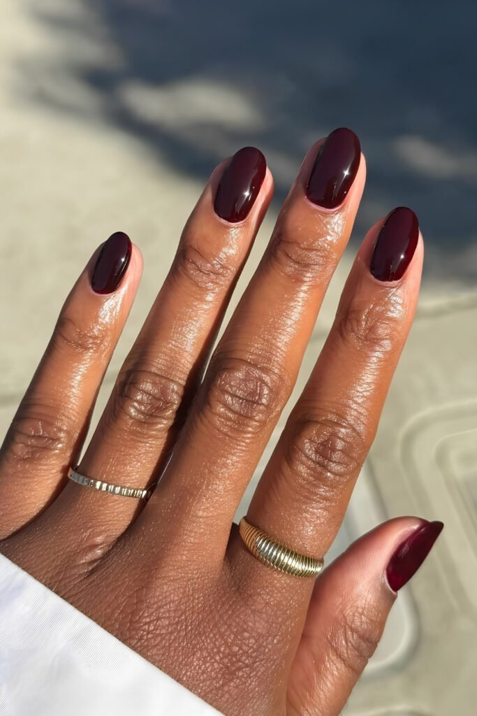 Short dark cherry nails on deep skin with gold rings