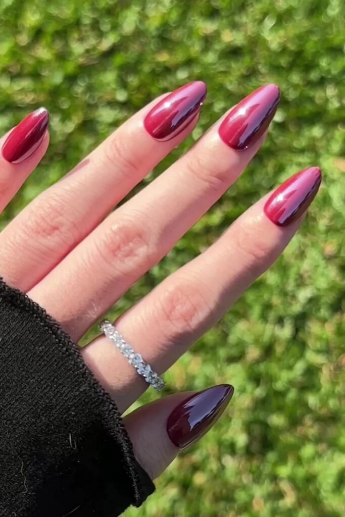 Glazed berry-red almond nails photographed over grass