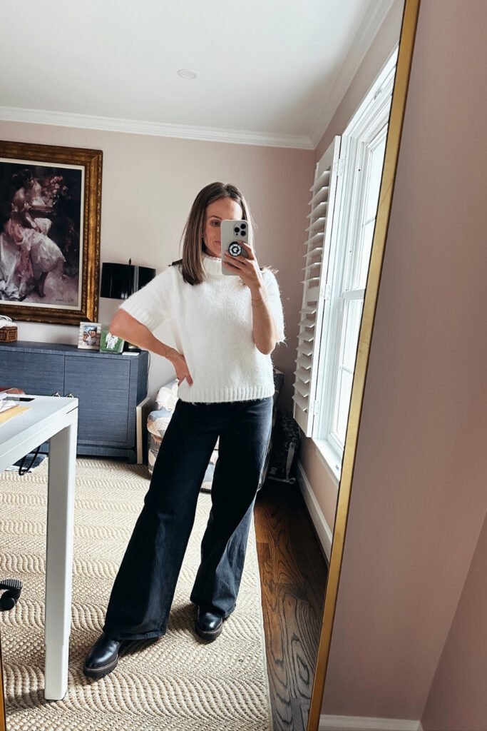 Woman in a white knit and wide-leg jeans taking a mirror selfie