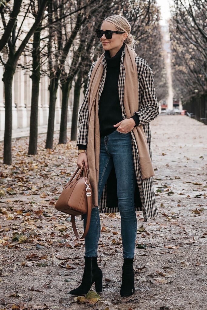 Woman in a coat and jeans with a tartan scarf on a leaf-covered path