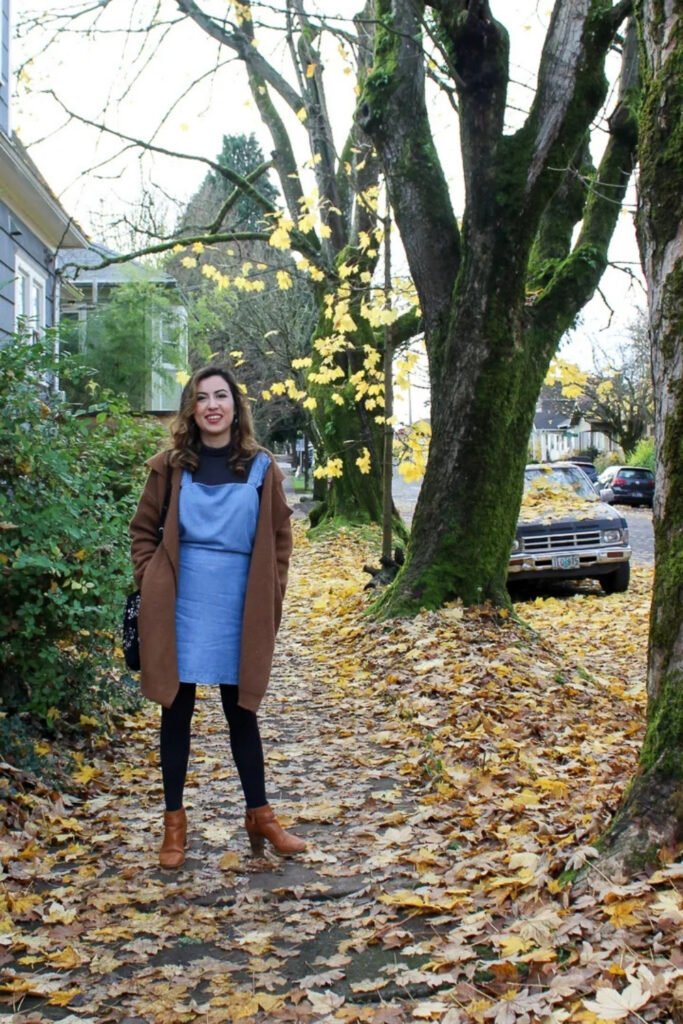 Woman in a blue pinafore dress with tights among autumn leaves