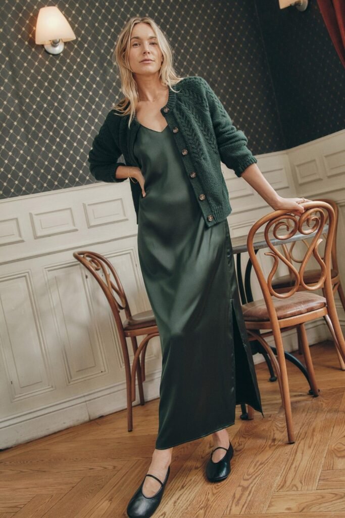 Woman in a green satin slip dress with a chunky knit cardigan