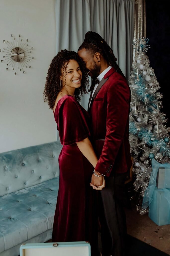 Couple in burgundy velvet beside a Christmas tree