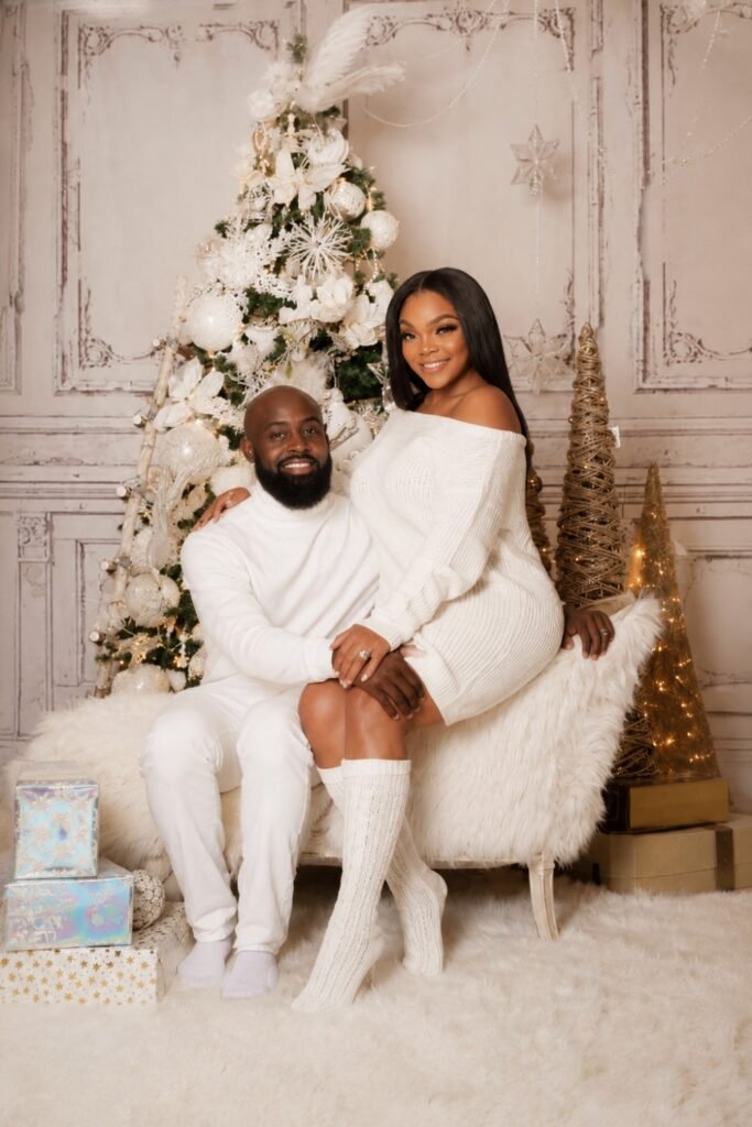 Couple in white outfits seated by a white Christmas tree