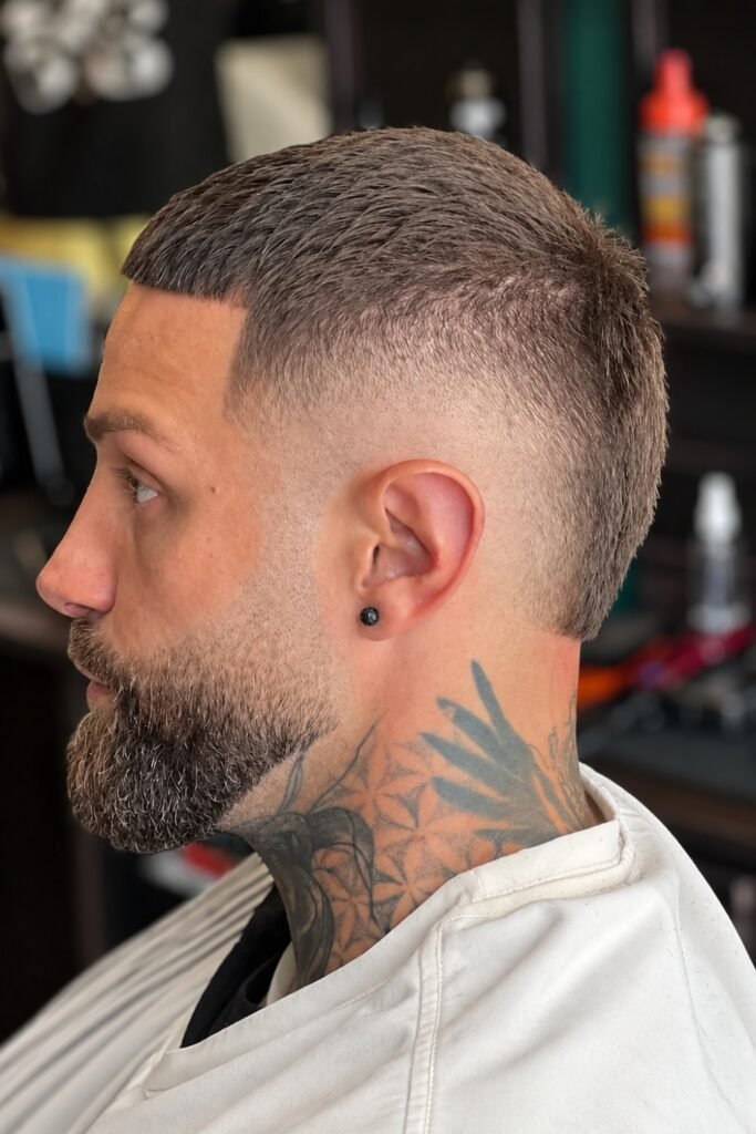 Buzz cut with a burst fade around the ear, worn with a beard
