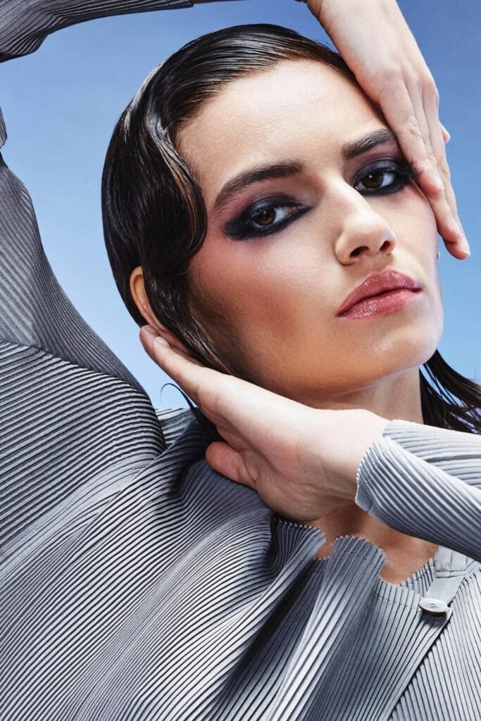 Cool-toned smoky eye makeup with slicked hair against a blue sky