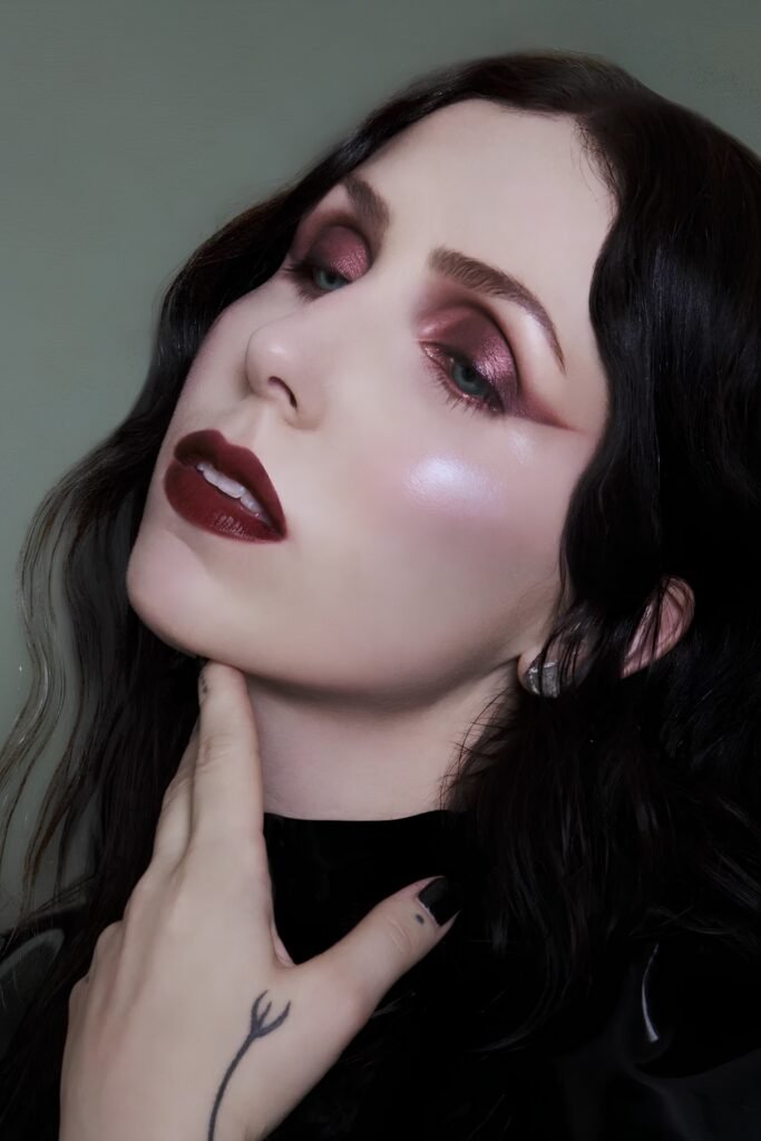 Pale skin with rosy-red eyeshadow and dark berry lips, hand resting at the neck