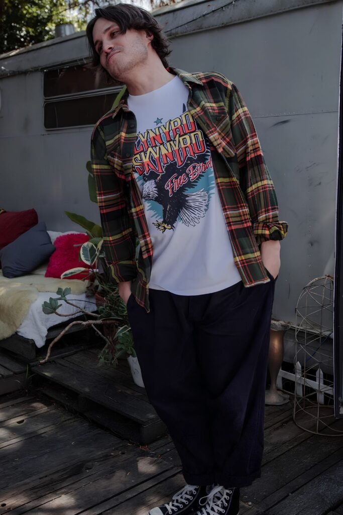 Man in an open dark flannel over a band tee with black jeans