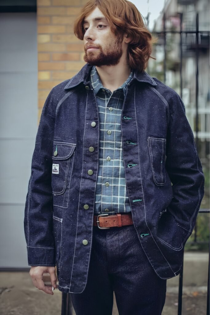 Man in a flannel shirt under a navy chore coat with raw denim