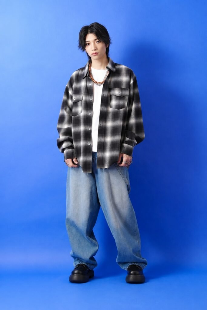 Man in an oversized plaid flannel with baggy jeans against a blue backdrop