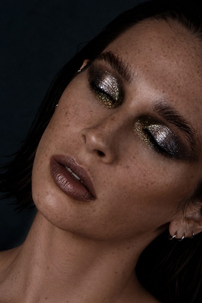 Close-up of a closed eye with fine shimmer on the lid, freckles and dark lips