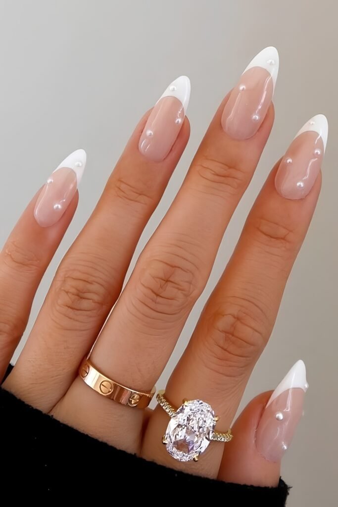 French almond nails with tiny pearl accents and a large oval ring