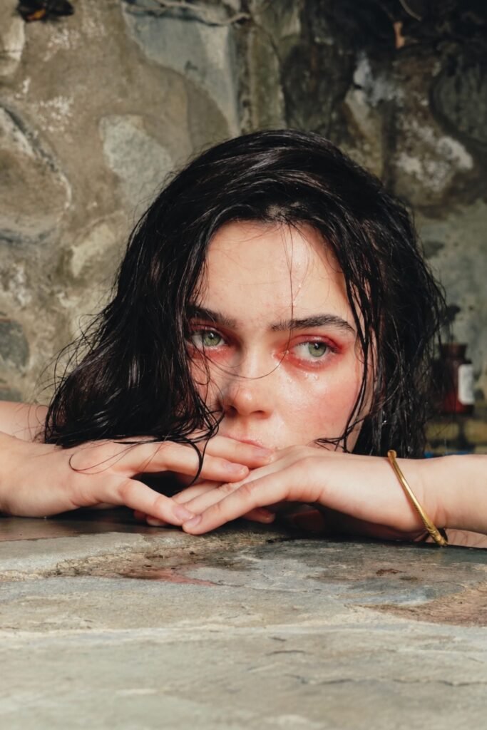 Smudged smoky eyes and damp dark hair, chin resting on folded arms
