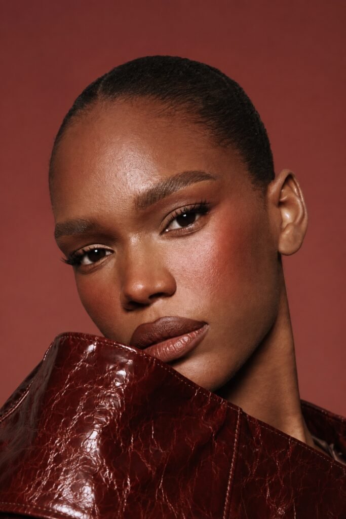 Deep skin with a warm flushed cheek, worn with a red-brown leather jacket