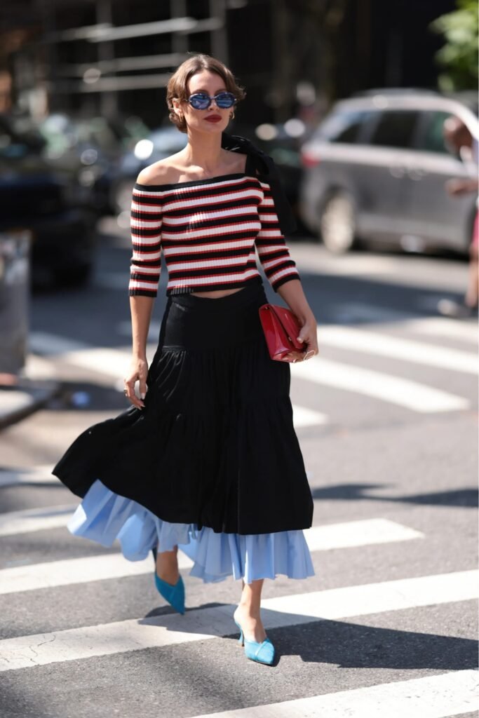 Woman with a cropped haircut crossing a street in a striped top and black skirt