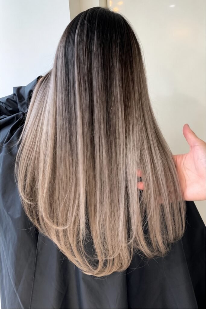 Back view of straight hair fading from dark roots to beige blonde ends
