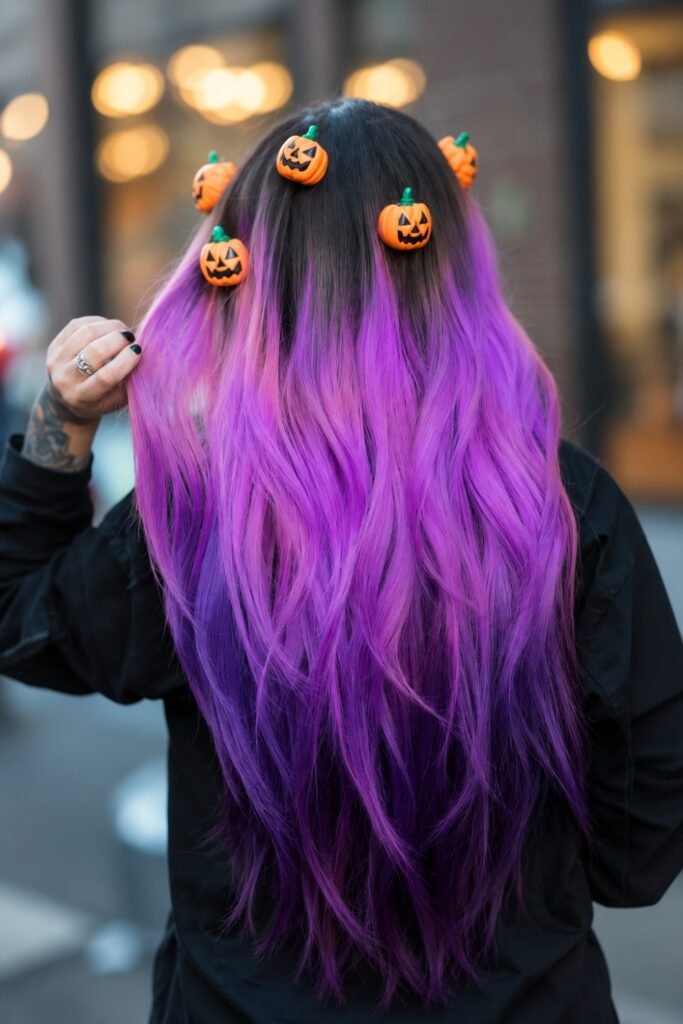 Back view of long wavy hair fading from dark roots to violet, with small pumpkin clips