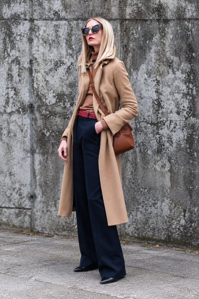 Woman in a camel coat with tortoiseshell sunglasses and a brown bag