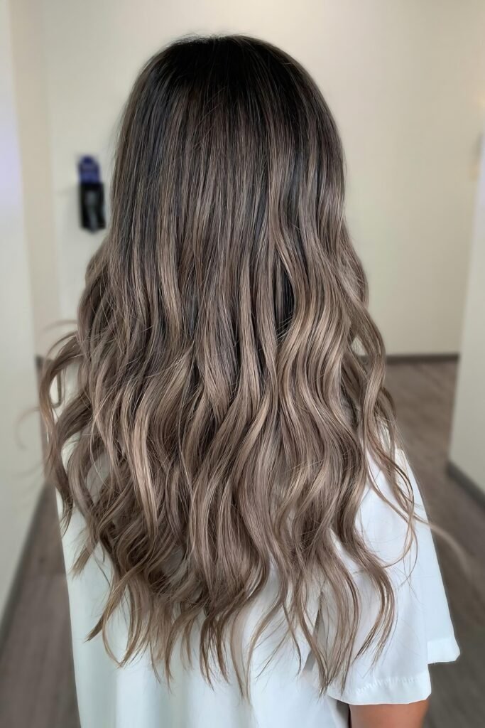 Back view of wavy hair fading from dark roots to milk tea ends